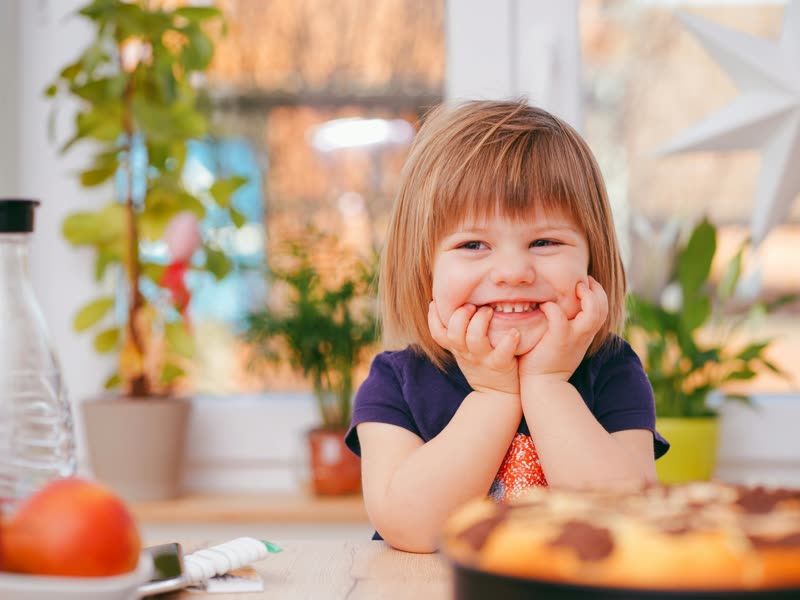 Une petite fille sourit, les mains sur les joues, devant son gâteau
